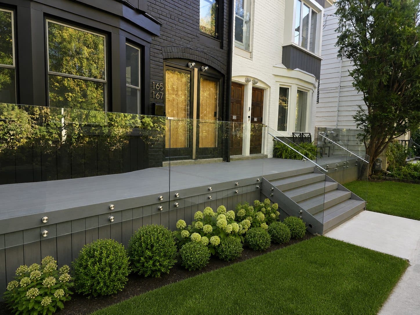 Shared front entrance deck spanning four Toronto row houses with frameless glass railings and planted borders
