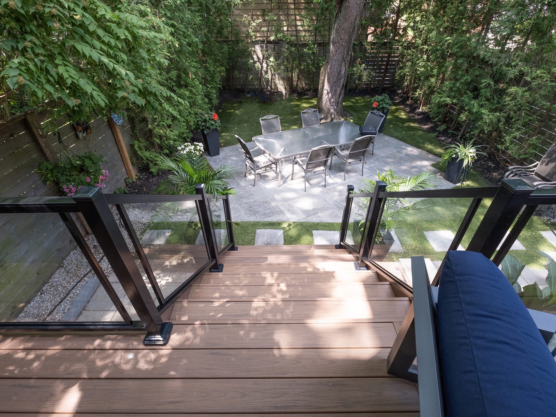 View down composite deck stairs to a stone patio and artificial grass yard